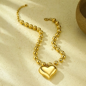 Detailed view of a 3D gold heart pendant with a polished bead chain on stone surface