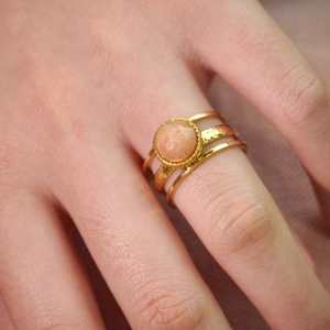 Macro detail of three layered gold rings featuring a faceted orange gemstone and hammered texture