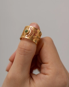 Detailed view of hollow floral pattern ring with green stone on a finger