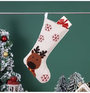 Détail d'une chaussette de Noël en lin avec broderie renne et boîte cadeau sur l'arbre