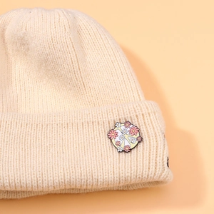 Cream knit beanie featuring a decorative floral and heart metal badge accessory