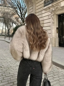Rear view of a beige faux fur jacket styled with black jeans in a street scene