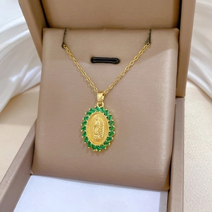 Macro detail of oval gold pendant with Virgin Mary relief and green crystal stones