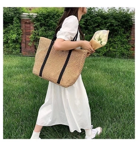 Outdoor shot of a beige woven tote bag with black canvas straps on a green lawn