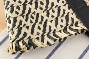 Macro view of multi-color woven straw bag featuring black and beige V-shaped patterns and fringe