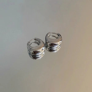 Gros plan des boucles d'oreilles huggie en forme de U argentées sur surface réfléchissante