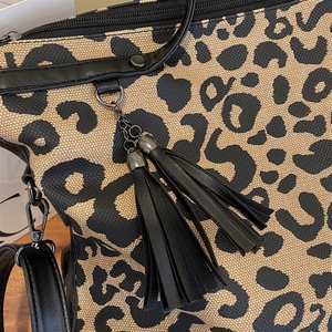Detailed close-up of leopard print canvas bag featuring leather tassels and metal buckles
