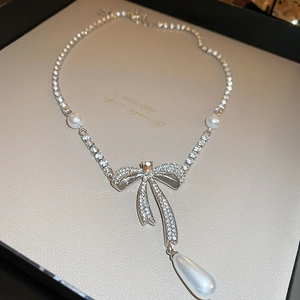 Close-up of sparkling zircon bow and teardrop pearl pendant on a silver-tone chain