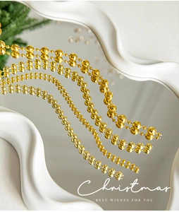 Golden Christmas bead garland on a white mirror surface with festive pine needle accents