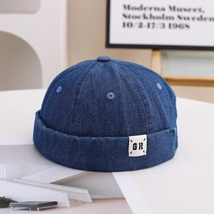 Detailed close-up of dark blue denim docker hat with GR logo label on a white table