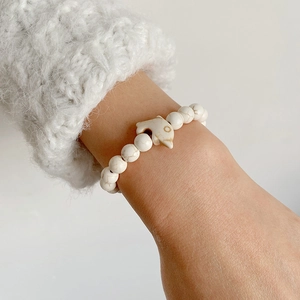 Detail of white beaded stone bracelet with a silver fish charm on a model's wrist