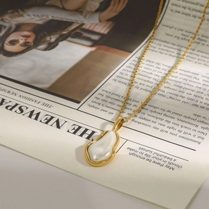 Detailed shot of golden twisted chain necklace with pearl pendant on a vintage newspaper