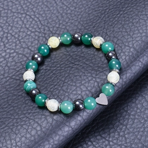 Detail of beaded bracelet with green stones and silver heart charm on black leather