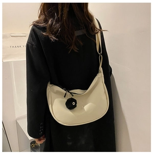 Model wearing a minimalist cream crescent crossbody bag with a black plush charm detail