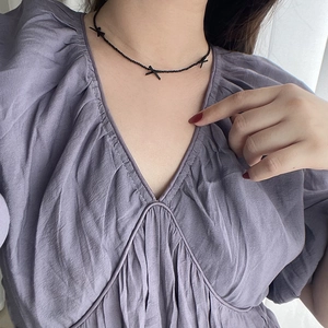 Close-up of black beaded necklace with small cross charms on a model wearing purple
