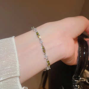 Detailed close-up of a silver bracelet with green teardrop gems and clear square zircons