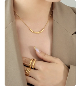 Gros plan d'un collier sourire doré et de bagues martelées portés sur un mannequin