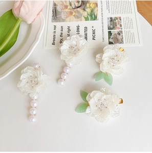 Dettaglio dei fermagli per capelli a camelia con perle e foglie su base bianca