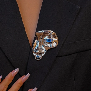 Détail macro d'une broche masque surréaliste argentée sur le revers d'un blazer noir