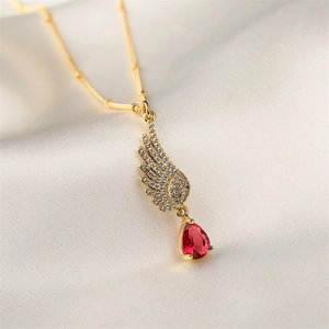 Macro shot of gold angel wing pendant with clear crystals and a pear-cut red gemstone