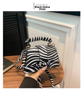 Detail of zebra pattern black handbag with gold hardware on a wooden table