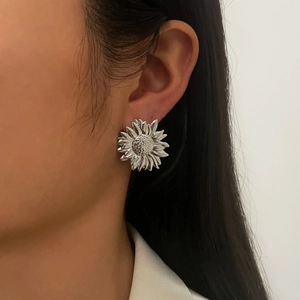 Close-up of a silver sunflower stud earring worn by a model on a neutral background