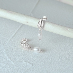 Detailed view of silver teardrop pearl earrings with white zircon on a wooden display
