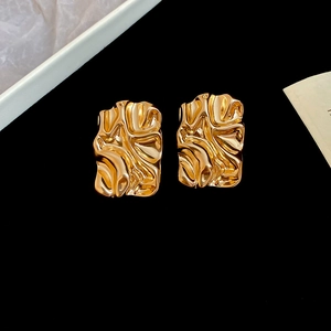 Macro shot of gold-plated rectangular earrings with textured liquid metal surface finish