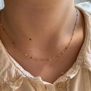 Gros plan d'un collier en chaîne dorée avec des perles colorées porté au cou