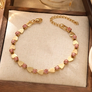 Detailed macro of gold heart charm and pink gemstone on an adjustable chain bracelet