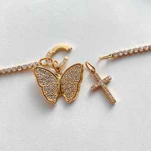 Dettaglio di ciondoli a farfalla e croce placcati oro 14K su una catena tennis di diamanti.