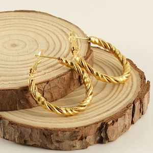 Golden stainless steel spiral twist hoop earrings displayed on natural wood slices