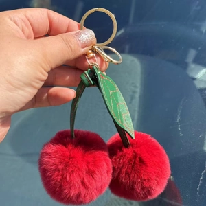 Close-up of cherry bag charm with red rabbit fur pom poms and golden keychain hardware