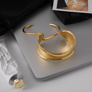 Bracelet jonc ouvert en acier plaqué or 18k et gourmette minimaliste sur un ordinateur argent