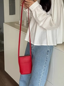 Red mini crossbody phone bag in leather worn by a model in a minimalist home setting