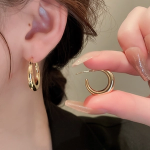 Detailed view of polished golden C-shaped hoop earrings on ear and held by hand