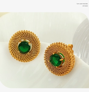 Close-up of vintage gold woven earrings with green gemstone inlay on ceramic plate