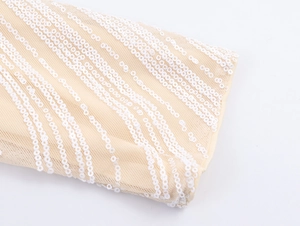 Detail of white sequins on skin-tone mesh fabric with wave patterns on the dress