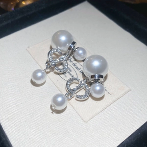 Macro detail of silver tone CD letter earrings with pavé zircons and dangling white pearls