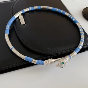 Detailed view of silver and blue snake-shaped bracelet with green gemstone eyes