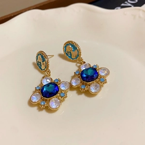 Detailed view of vintage gold flower earrings with blue rhinestones on a beige plate