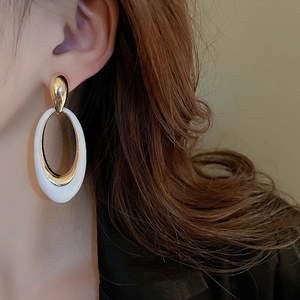 Macro view of exaggerated oval drop earrings with white enamel and golden metal finish