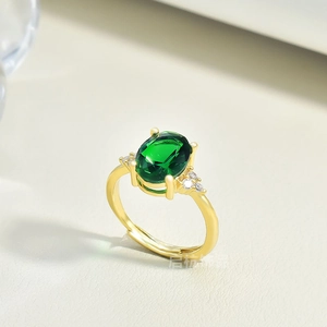 Detail of adjustable gold ring with oval emerald gemstone and side zircon accents