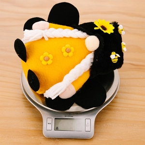 Detailed view of handmade bee gnome plush on scales showing light 143.3g weight