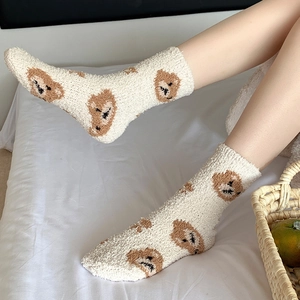 Close-up of soft coral fleece socks with cute brown bear patterns in a cozy bed setting
