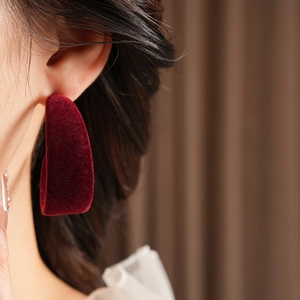 Close-up of elegant deep red velvet C-shaped earrings worn by a model in soft lighting