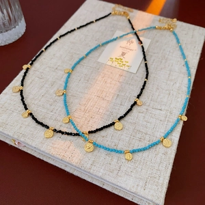 Détail de colliers de perles ethniques avec pendentifs pièces dorées sur tissu beige