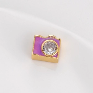 Dettaglio di un ciondolo a forma di fotocamera dorata con smalto viola e cristallo