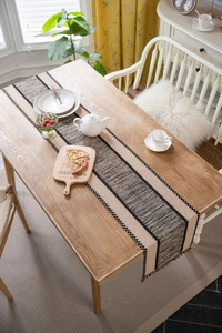 Detail of hand-woven table runner with beige and black contrast stitching and fringes