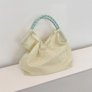 Detailed embroidery of white flowers on a light green mesh tote bag with woven handles